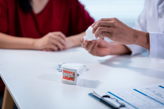 Dentist showing a dental implant model to a patient during a clinic consultation, with jaw model and paperwork on the desk in a clean modern office.
