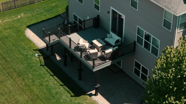 Aerial view of Modern elevated backyard deck attached to suburban house featuring black metal railings, outdoor stairs, and covered patio space in residential neighborhood