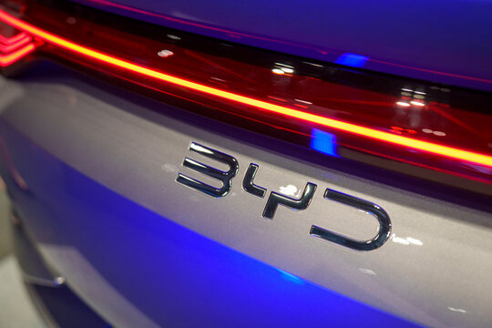Penang, Malaysia - May 02, 2026: A close-up shot of the chrome BYD emblem on the metallic grey rear body of an electric car, featuring an illuminated red LED taillight bar in a showroom.