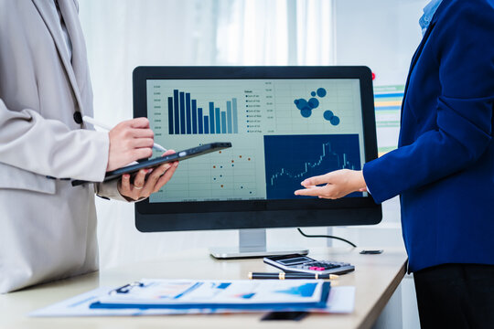 Experienced Asian woman trains new employee in office work, teaching secretarial duties, document management, assistant manager responsibilities. She guides workplace procedures at the office desk.