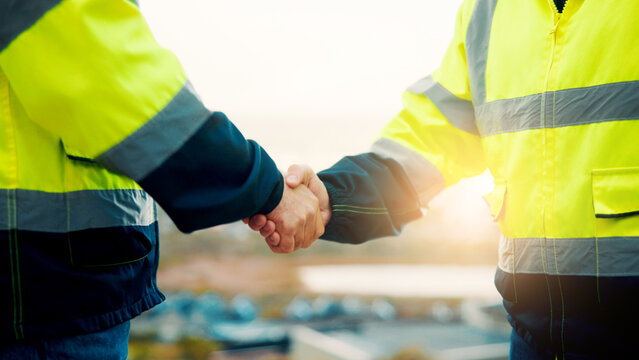 People, engineer and meeting with handshake on rooftop for building deal or partnership in city. Contractor, builder or shaking hands with flare for teamwork or agreement on construction site