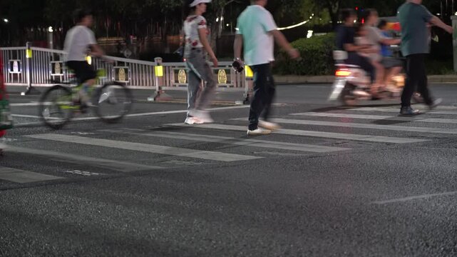 Blurred Pedestrians and Cyclist Crossing City Street at Night