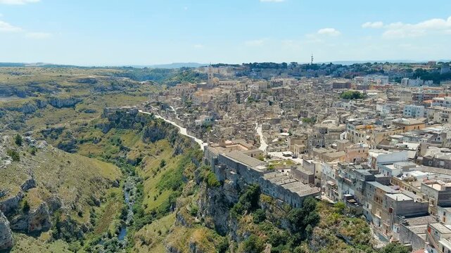 Matera, Italy. The ancient Sassi cave dwellings, a dense cluster of stone houses carved into limestone cliffs, aerial panoramic view on a bright summer day. Drone footage