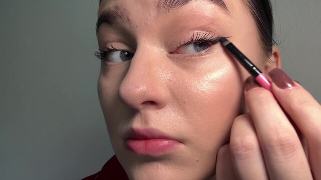 Woman applying winged eyeliner, shaping eye makeup, demonstrating cosmetic technique, self-care routine, cosmetology practice, using an applicator, groomed eyelashes, natural lips, glowing skin.