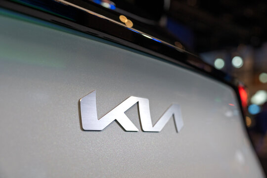 Penang, Malaysia - May 02, 2026: A close-up detailed shot of the brushed aluminum Kia emblem mounted on the metallic pearl white rear tailgate of a Kia Sportage SUV at an automotive exhibition booth.