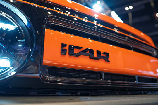Penang, Malaysia - May 02, 2026: A close-up shot of the front fascia of an orange Chery iCAR V23 electric vehicle, showcasing the embossed black "iCAR" wordmark logo on a vibrant orange panel.