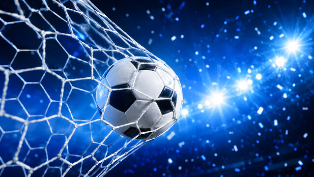 Soccer ball flew into the goal. Soccer ball bends the net, against the background of flashes of light. Soccer ball in goal net on blue background 