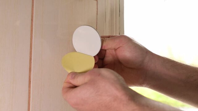 Man sticks self-adhesive metal hook to tile and hangs a purple towel. Installation of a wall-mounted metal hook on an adhesive base near the window on tiles, home comfort, organization of space
