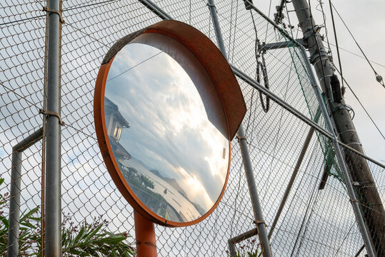 Scenic Sea and Sunset Sky Reflected in a Rusty Roadside Convex Traffic Mirror by a Wire Fence
