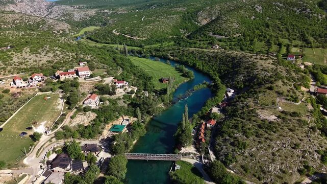 Aerial view of Slapovi Zrmanja and the Zrmanja river winding through the valley with houses and a bridge in Muskovci, Zadarska zupanija, Croatia.