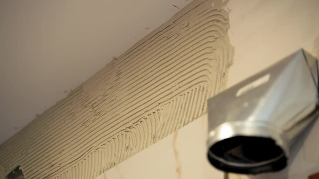 Professional worker applies thick layer of adhesive to ceramic tile to glue on wall. Close up
