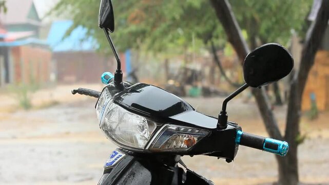 Cinematic Close Up of Delicate Wilderness Sylvan Foliage Blurred Behind Wet Handlebars with Rain on a Motorcycle in the Park in 4K Slow Motion