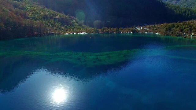 Serene Turquoise Mountain Lake with Forest Shoreline and Sun Reflection