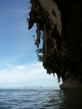 View to the tropical sea from the shade of a massive mogote karst overhang with stalactites on Koh Panak in Thailand