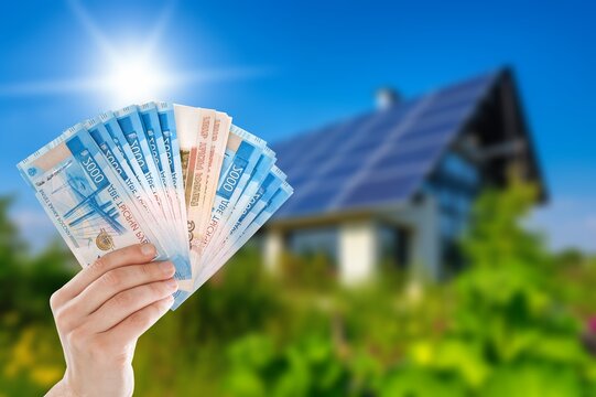 Person holding Russian ruble banknotes in front of house with solar panels
