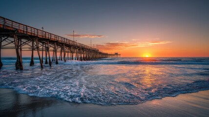 Fototapeta premium Sunset at pier with waves crashing on the shore in California during late evening hours