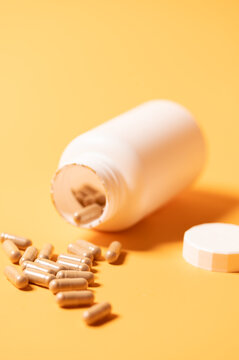High-angle close up of an open white plastic pharmaceutical bottle with scattered medical capsules on a bright yellow surface. Concept of dietary supplements, vitamins, healthcare, and prescription me