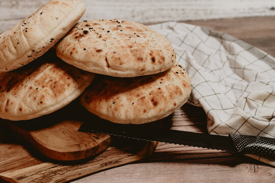Stack of freshly baked pita bread flatbreads on a wooden table.Traditional homemade flatbread loaves with black cumin seeds on wood.Close-up of golden brown grilled pita breads with rustic kitchen clo