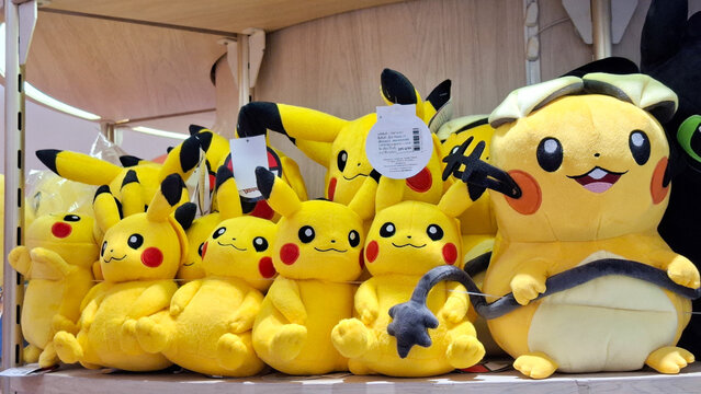 Group of yellow pikachu plush toys in various sizes sitting together on a wooden shelf inside a gift shop on May 13, 2026 in Bangkok, Thailand.