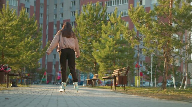 Teenage girl rollerblading in urban park during golden hour sunset light on pavement.