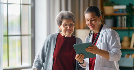 Smiling Female Doctor Consults Happy Senior Woman at Home with Digital Tablet