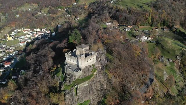 Aerial view of Castel Grande historic stone fortress on a rocky outcrop surrounded by autumn trees and houses in Bellinzona, Ticino, Switzerland.