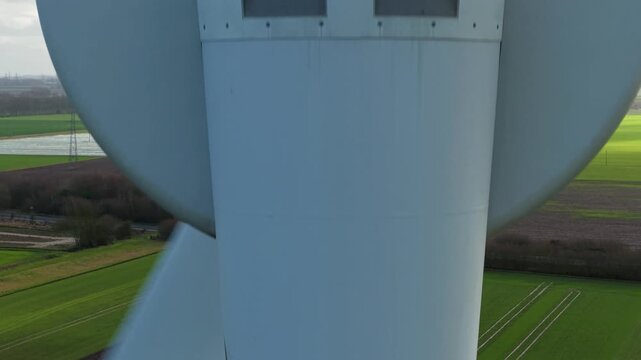High angle aerial view framing a single modern wind generator spinning over green rural fields