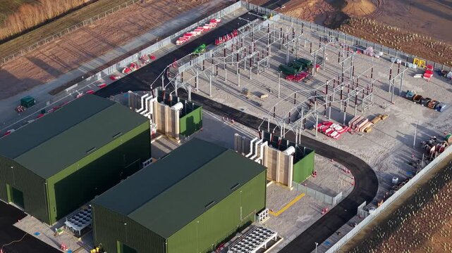 90 degree overhead drone shot of industrial metal busbars pylons transformers and containerised battery systems