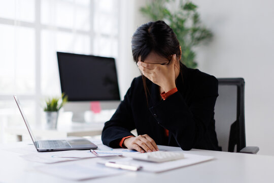Stressed business woman feeling overwhelmed and frustrated, needing a break from intense work pressure, experiencing burnout, exhaustion, and chronic headache in a modern office