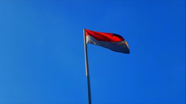 A flag with red on top and white on the bottom flutters against a blue sky. The flag of Indonesia. The flag of Monaco.