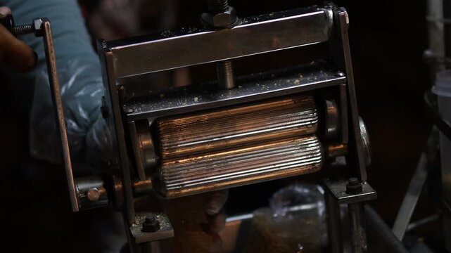 Close-up of a street food vendor using a traditional metal roller machine to crush and flatten dried squid, illustrating authentic Asian street food preparation and local culinary culture