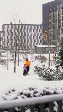 Parent and child decorating snowman in snowy city park in winter
