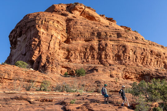 Two hikers descend a massive red rock formation