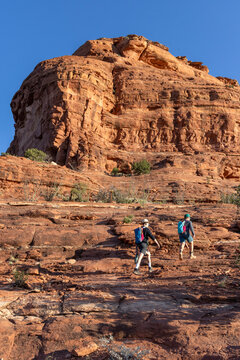 Two hikers traverse a sunny red rock landscape