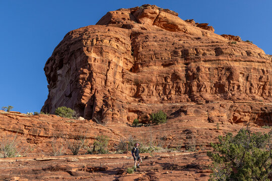 Lone hiker pauses below a massive red rock cliff