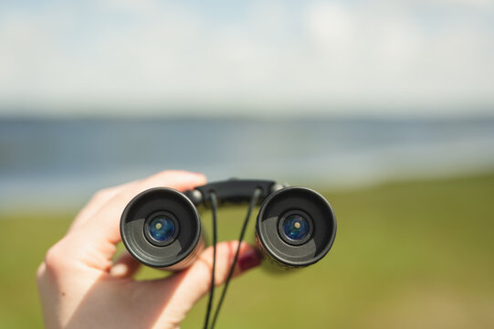 Hand holding binoculars overlooking blurred nature with copy space