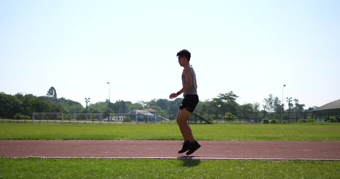 Cinematic wide shot of a male athlete doing butt kicks running drills on an outdoor track, running form conditioning concept