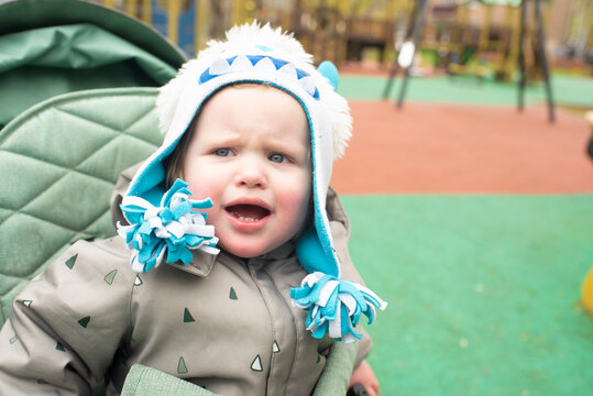Crying toddler sitting in green stroller showing upset face expression outdoors