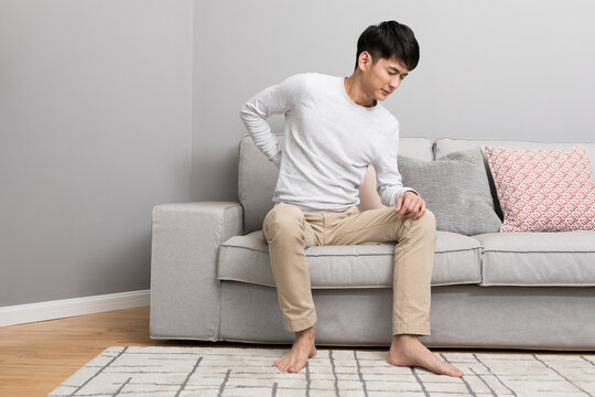 Young man with lower back pain sitting on sofa at home