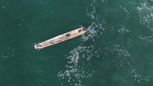 Aerial view of a traditional wooden fishing boat floating on the turquoise sea water with white foam in Kovalam, Kerala, India.