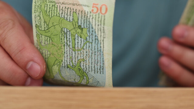 Horizontal defocused photo close up. Georgian cash money. Male hand counts green paper banknote fifty lari bill, 50 GEL on wood table. Concept of pay tax, loan, debt, salary, wages, credit, budget