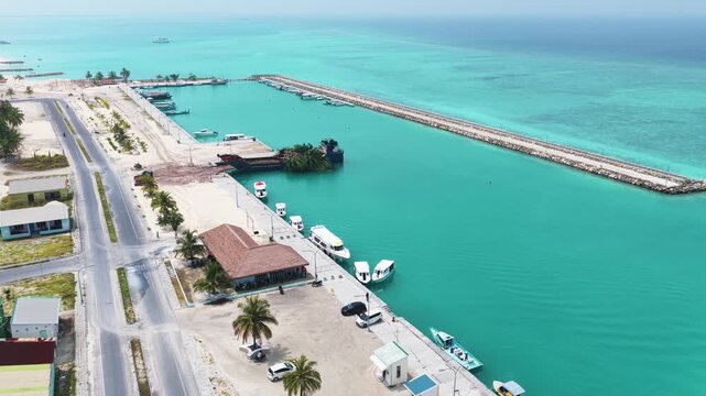 Aerial view of a harbor with boats docked along the pier, turquoise water and a long breakwater under a clear sky in Hanimaadhoo, Haa Dhaalu, Maldives.