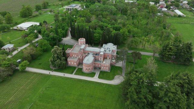 Aerial view of Chateau Mukhrani royal palace and estate in Georgia, magnificent pink castle architecture with a tower surrounded by a lush green park, gardens and pathways on a spring day.