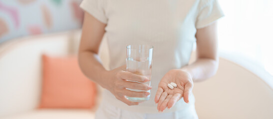 Obraz premium woman hand holding medicine painkiller pill and water glass on the sofa at home, taking for headaches, stomach ache, Diarrhea Pain from food poisoning, Endometriosis, Hysterectomy and Menstrual