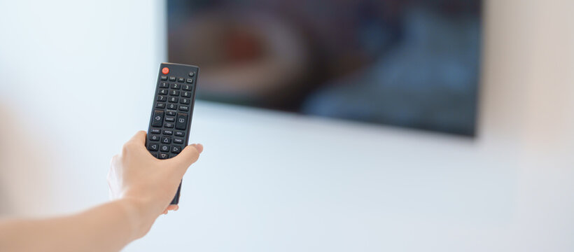hand using remote controller press button for adjust Smart TV in modern room at home. Woman holding remote control,  switch channel, searching new interesting program, Turn on or off on Television