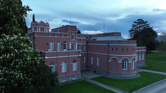 Aerial view of Chateau Mukhrani royal palace and estate in Georgia, magnificent pink castle architecture with a tower surrounded by a lush green park, gardens and pathways on a spring day.