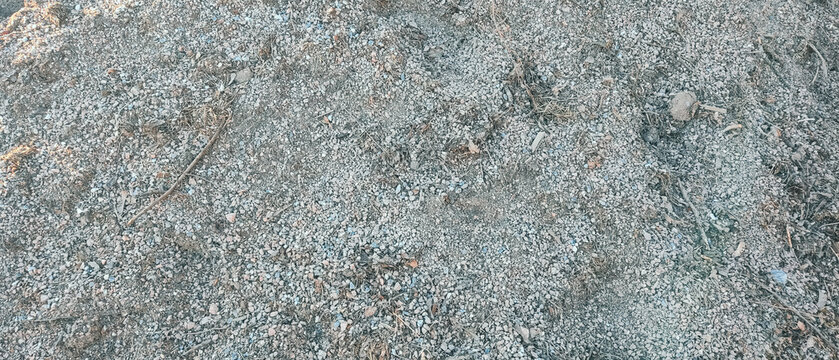 High-angle background shot of natural grey crushed stone aggregate mixed with dry organic debris, dirt, and small twigs. Perfect for construction, landscaping, gardening, or textured abstract backgrou