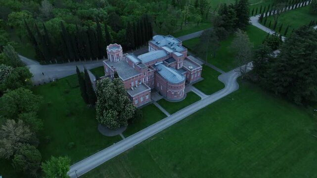 Aerial view of Chateau Mukhrani royal palace and estate in Georgia, magnificent pink castle architecture with a tower surrounded by a lush green park, gardens and pathways on a spring day.