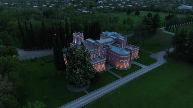 Aerial view of Chateau Mukhrani royal palace and estate in Georgia, magnificent pink castle architecture with a tower surrounded by a lush green park, gardens and pathways on a spring day.