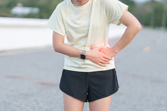 Adult runner suffering from side stitch and waist pain during exercise. woman holding his side due to sharp abdominal cramp or muscle ache while running. Sports injury and healthcare concept